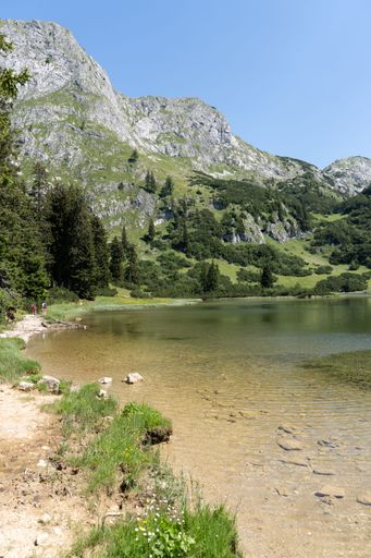 A vertical shot of a mountain lake with two people near the shore