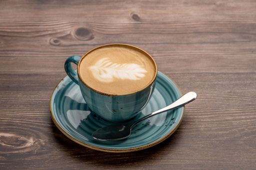 A cappuccino with latte art in a blue cup served on a wooden table