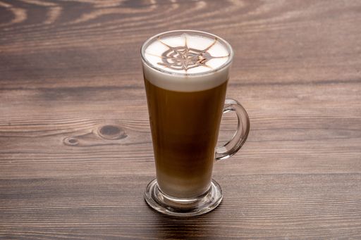 A coffee with foam in a glass cup served on a wooden table