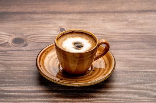 A cappuccino with latte art in a brown cup served on a wooden table