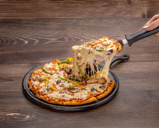 A woman's hand taking a slice of a large pizza with melted cheese and peppers with a peel