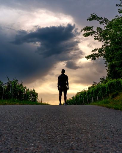 A vertical shot of a silhouette of a man standing alone in the middle of a road under a cloudy sky