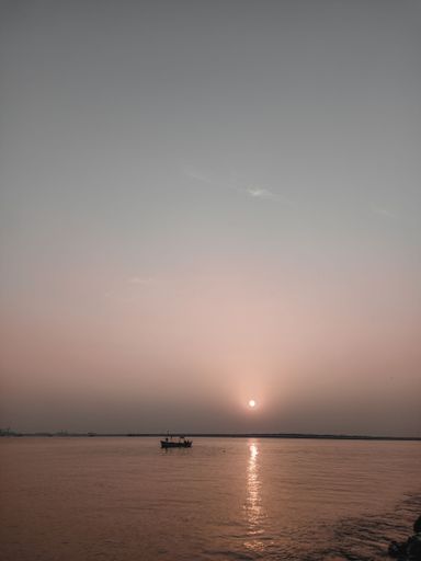 A vertical silhouette of a boat floating in the ocean during sunset