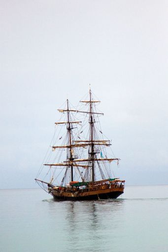 A vertical shot of two-masted wooden ship sailing in the sea under cloudy sky