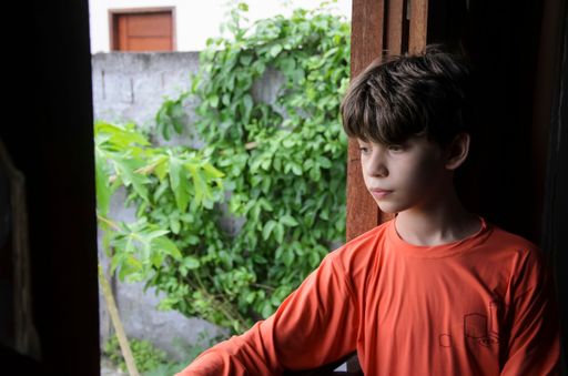 A Portrait of a Caucasian boy at the window wearing an orange shirt, Bahia, Brazil