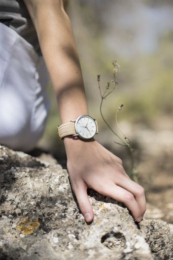 A vertical shot of the hand of a person with a watch touching a rock
