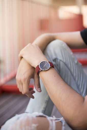 A vertical shot of the hands of a male with a red watch sitting on the ground