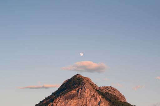 A low angle shot of a top of a mountain under the sky and a small image of the moon in the center
