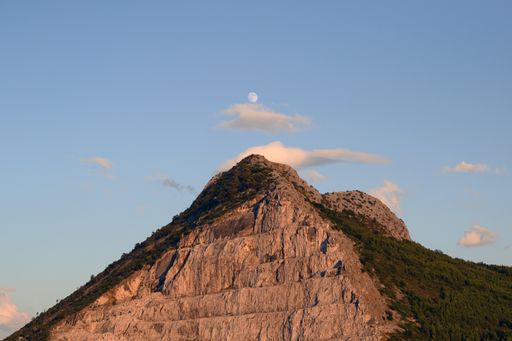 A low angle shot of the top of a hill under the bright sky and a small image of the day moon in the center