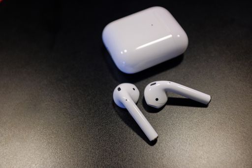 A closeup shot of a pair of air pods and a charging case on a black background