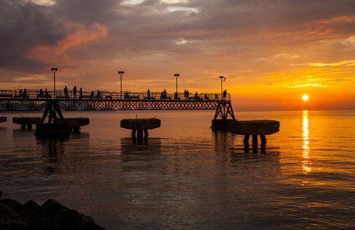 A breathtaking scenery of people sitting on benches of the bridge and admiring the sunset over the sea