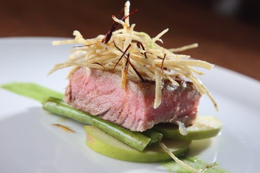 A closeup shot of medium roasted tuna loin with a garnish of apples and tortilla strips