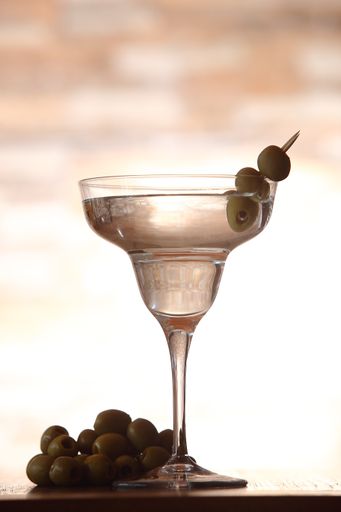 A vertical shot of a classic Martini with olives on a blurred background