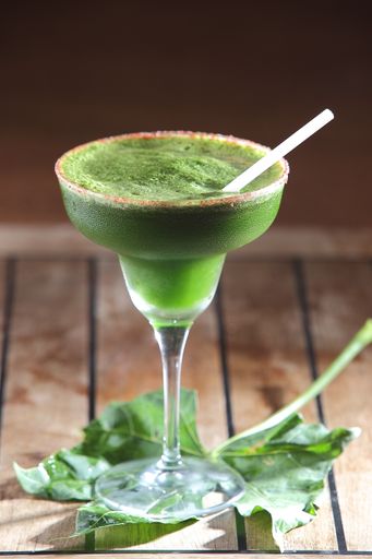 A selective focus shot of a glass of chaya cocktail with a straw on mint leaves