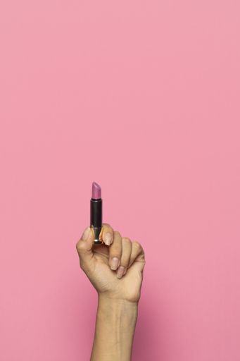 A vertical shot of a hand holding a lipstick isolated on a pink background