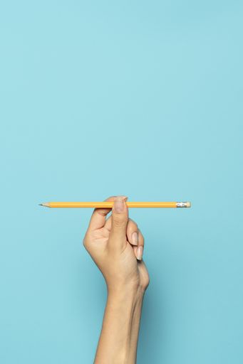 A vertical shot of a hand holding a pencil isolated on a blue background