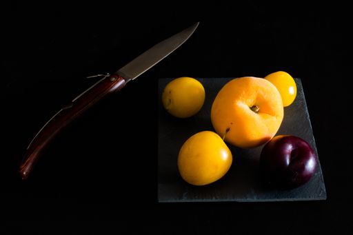 A high angle shot of some peaches and plums and a knife on a black surface