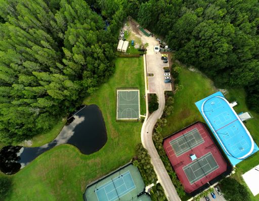 An aerial top view of professional courts of tennis and basketball surrounded by green forests