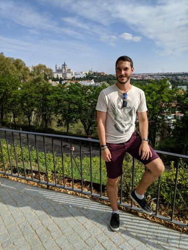 A portrait of a male leaning on a railing with the Almudena Cathedral in Madrid, Spain on the background