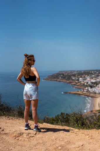 A vertical shot of a Caucasian Fitness model in sports bra and shorts overlooking a town in Portugal