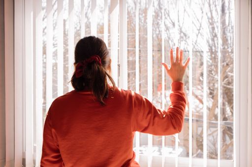A back view of a female looking out of the window blinds