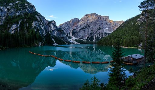 A scenic view of rural wooden houses on a shore of a lake near green pine forests and mountains