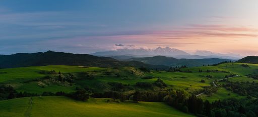 A panoramic view of a green landscape covered with forests and Tatra Mountains in Slovakia at sunset