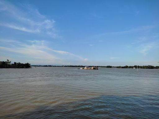 An aerial view lake with floating boat surrounded by trees under blue bright sky