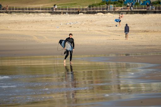 A young surfer with a surfboard walking down the beach in sunny weather