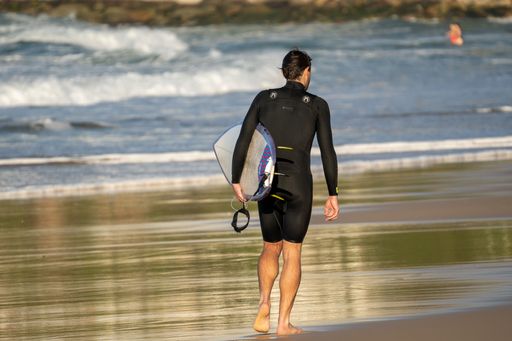 A young surfer from behind walking down the beach with his surfboard
