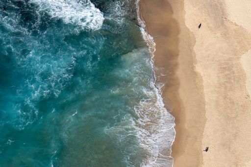 An aerial view of blue ocean waves hitting the beach in sunny weather