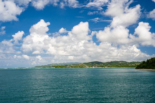 A landscape of the sea surrounded by hills covered in greenery under a blue cloudy sky