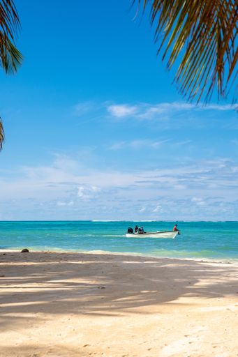 A vertical shot of a beach surrounded by the sea with a boat on it under the sunlight and a blue sky