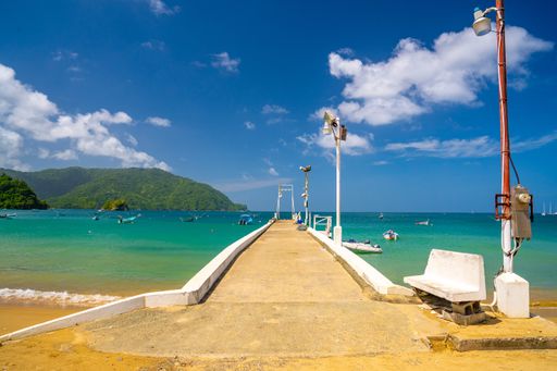 A dock on the sea surrounded by hills covered in greenery under the sunlight and a blue sky