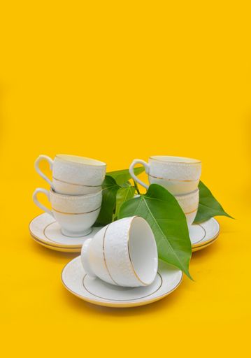 White porcelain tea cup with a golden line decoration and a saucer on yellow colour background with clipping path