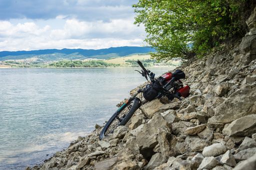 A bicycle with red panniers lying on the rocky beach of Czorsztyn Lake