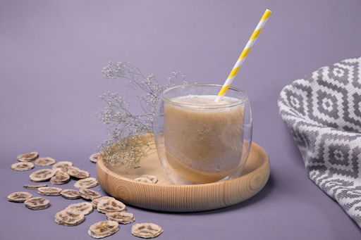 A glass of iced coffee with dried bananas next to it over a purple background