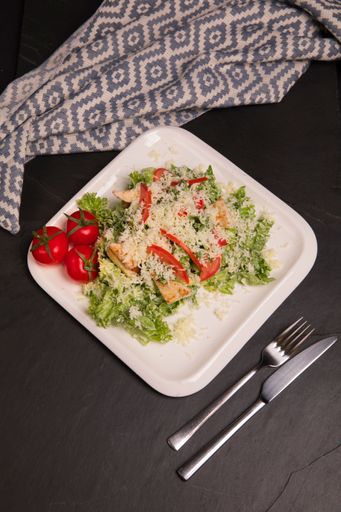 A top view of Cesar salad with a piece of clothing, fork and knife on the table