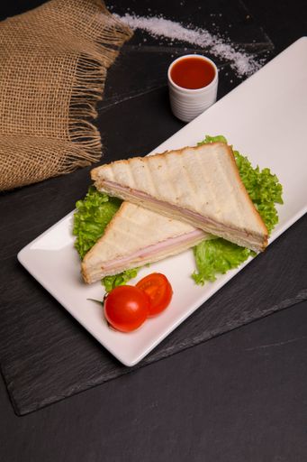 A closeup vertical shot of sandwiches with tomatoes on the white plate and sauce on the table