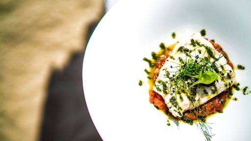 A closeup shot of white fish dish with basil pesto and garnish on a white plate