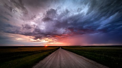 A road with fields on the both sides leading to the purple and cloudy sky