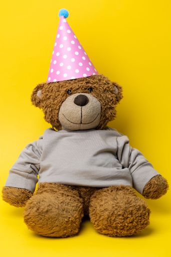 A vertical shot of a Cute Teddy Bear with a Party hat on yellow background.