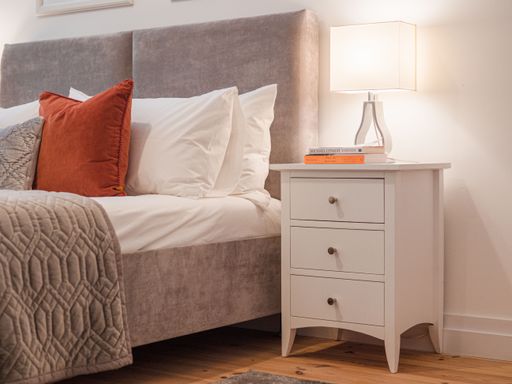 A closeup of a modern bedroom interior with a small white nightstand next to the bed