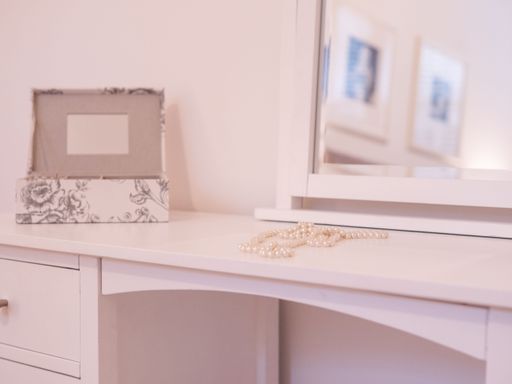 A selective focus shot of a pearl necklace and jewelry box on a white dressing table with a mirror