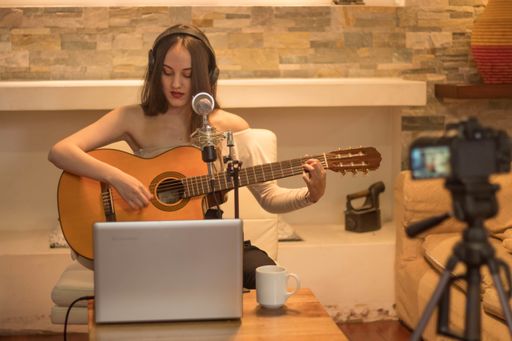 A closeup shot of a young female artist playing the guitar and singing while recording it