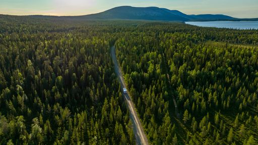 Aerial view following a Camper van, at lake Pallasjarvi driving towards Ounastunturit fells, summer evening in Pallas-Yllastunturi national park