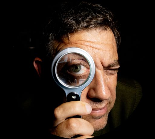 A comic portrait of a man holding a magnifying glass in front of his eye