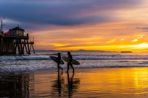 A beautiful shot of two people walking on a beach with surfboards at a yellow sunset