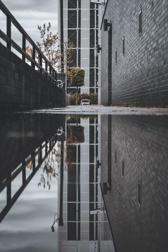 A vertical shot of a modern building reflecting in a puddle on a cloudy day