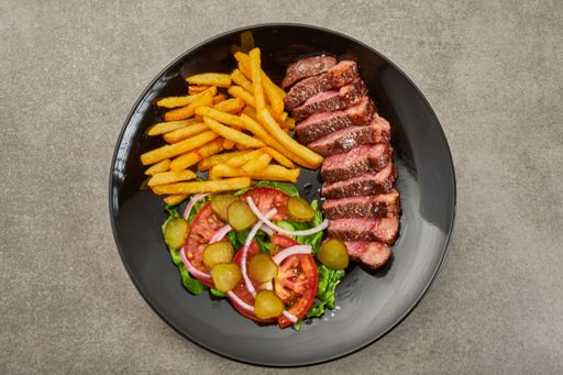 A top view of steak strands, fries and different vegetables on a black plate